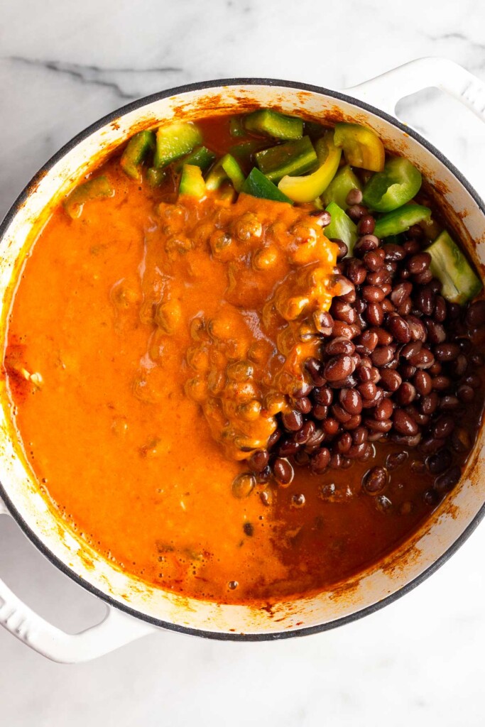 Soup with raw diced bell peppers, black beans, and a creamy chipotle sauce in a white dutch oven before it is mixed together.