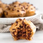 Cottage cheese muffin with a bite taken out of it. Behind it is plate of more muffins and sitting on a striped towel.