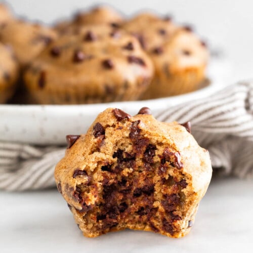 Cottage cheese muffin with a bite taken out of it. Behind it is plate of more muffins and sitting on a striped towel.