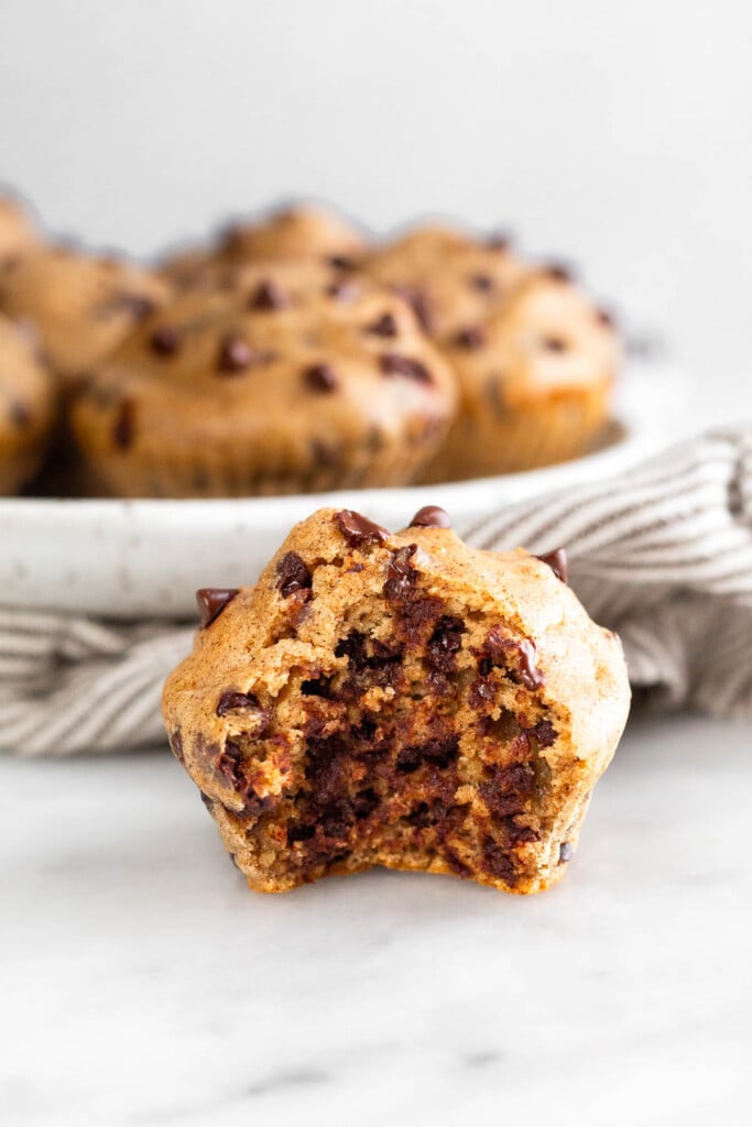 Cottage cheese muffin with a bite taken out of it. Behind it is plate of more muffins and sitting on a striped towel.
