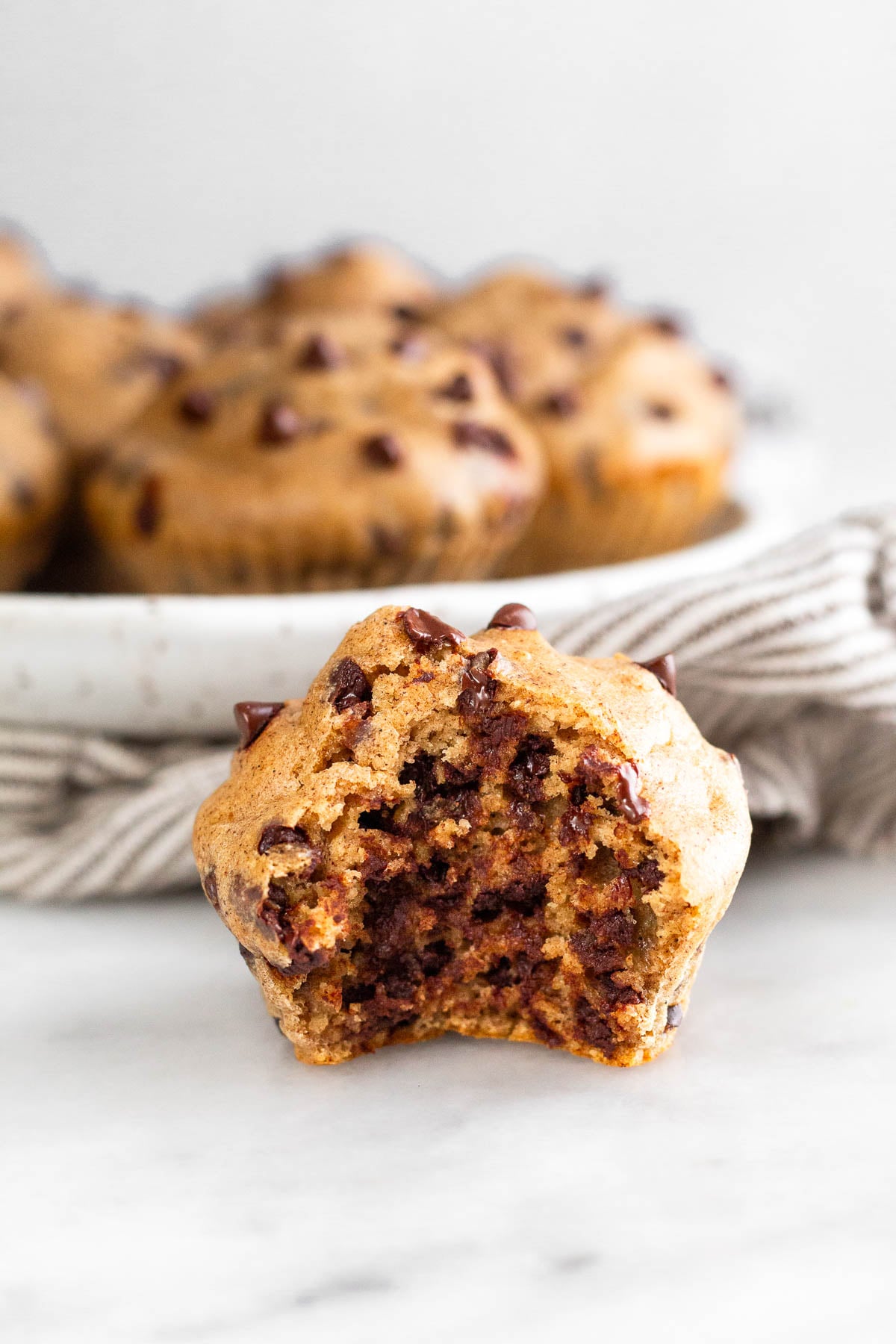 Cottage cheese muffin with a bite taken out of it. Behind it is plate of more muffins and sitting on a striped towel.