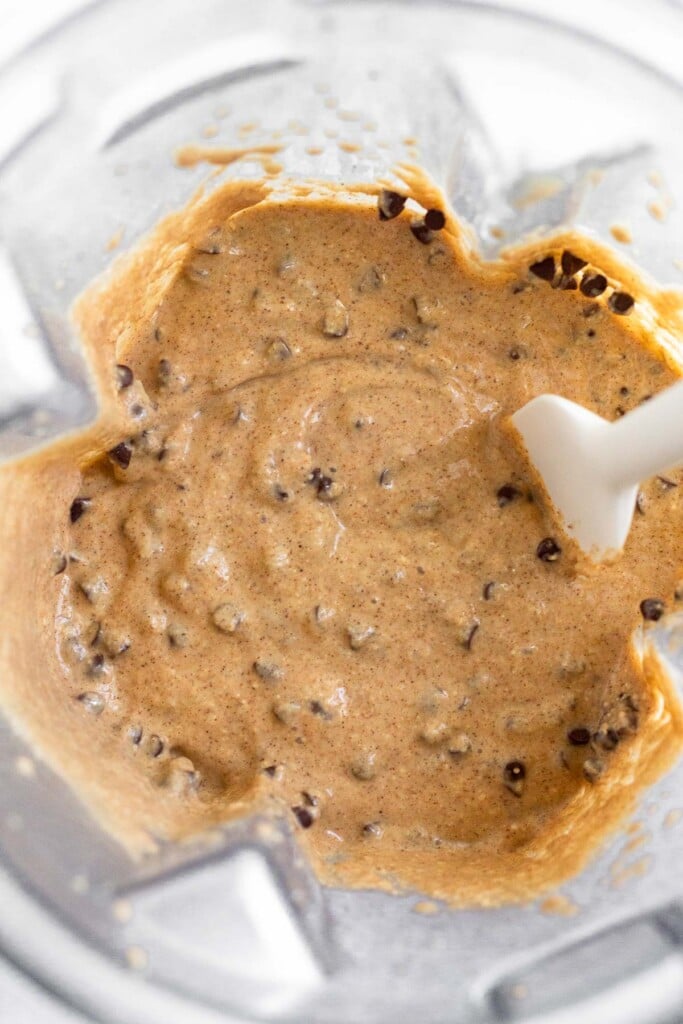 Wet batter with chocolate chips in it in a blender. A spatula is in the blender.