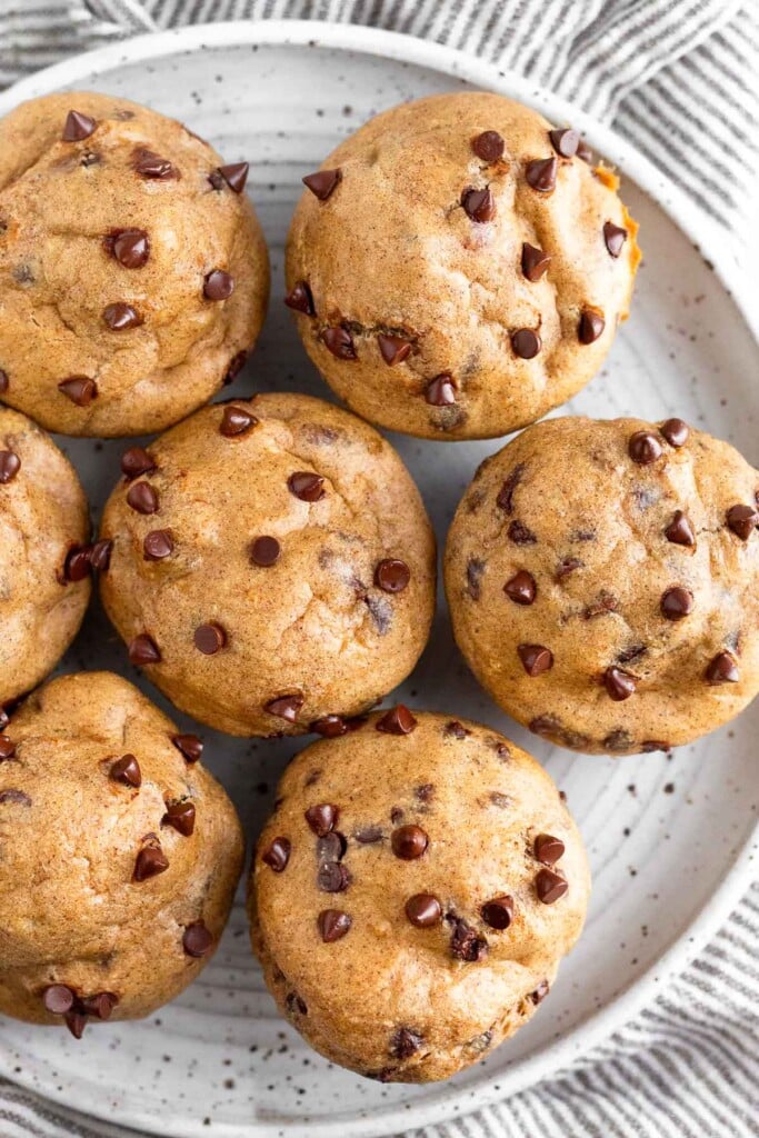 Overhead shot of chocolate chip cottage cheese muffins on a white plate that is sitting on a striped kitchen towel.