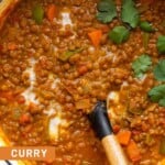 Curry lentil soup garnished with coconut milk and cilantro in a large white dutch oven with a spoon in it.