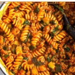 Large white dutch oven filled with ground turkey pasta with veggies. A spoon is also in the pot.