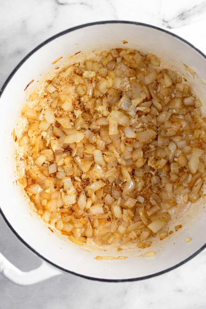 Large white dutch oven filled with sautéed onion and garlic.