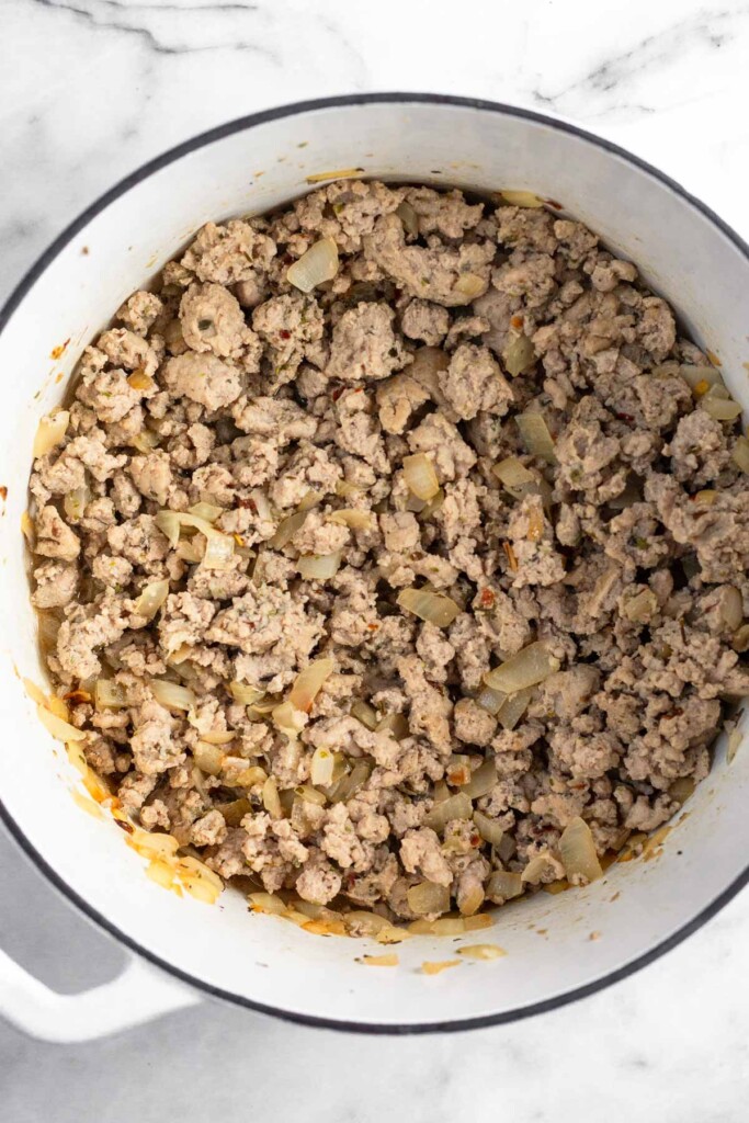 Large white dutch oven filled sautéed onion and seasoning ground turkey.