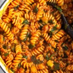 Large white dutch oven filled with ground turkey pasta with veggies. A spoon is also in the pot.