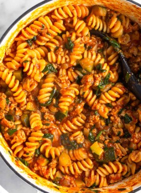 Large white dutch oven filled with ground turkey pasta with veggies. A spoon is also in the pot.