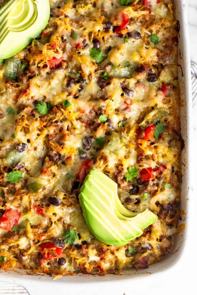 High protein beef spaghetti squash casserole recipe topped with sliced avocado and cilantro in a white baking dish.