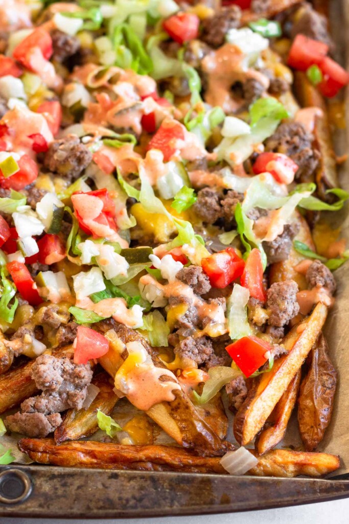 Cheeseburger fries on a large baking sheet. The fries are topped with ground beef, melted cheese, lettuce, tomato, pickles, and special sauce.