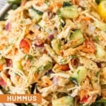 Hummus chicken salad overtop greens in a white bowl.