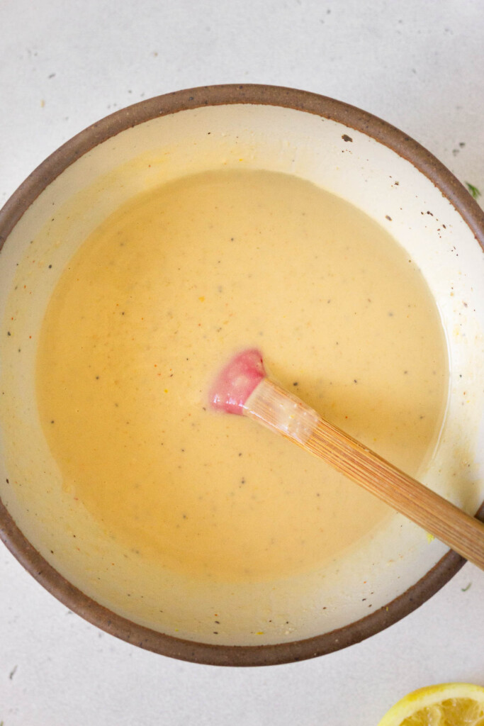 Bowl of a hummus dressing with a spatula in it. Next to the bowl is half a lemon that has been juiced.