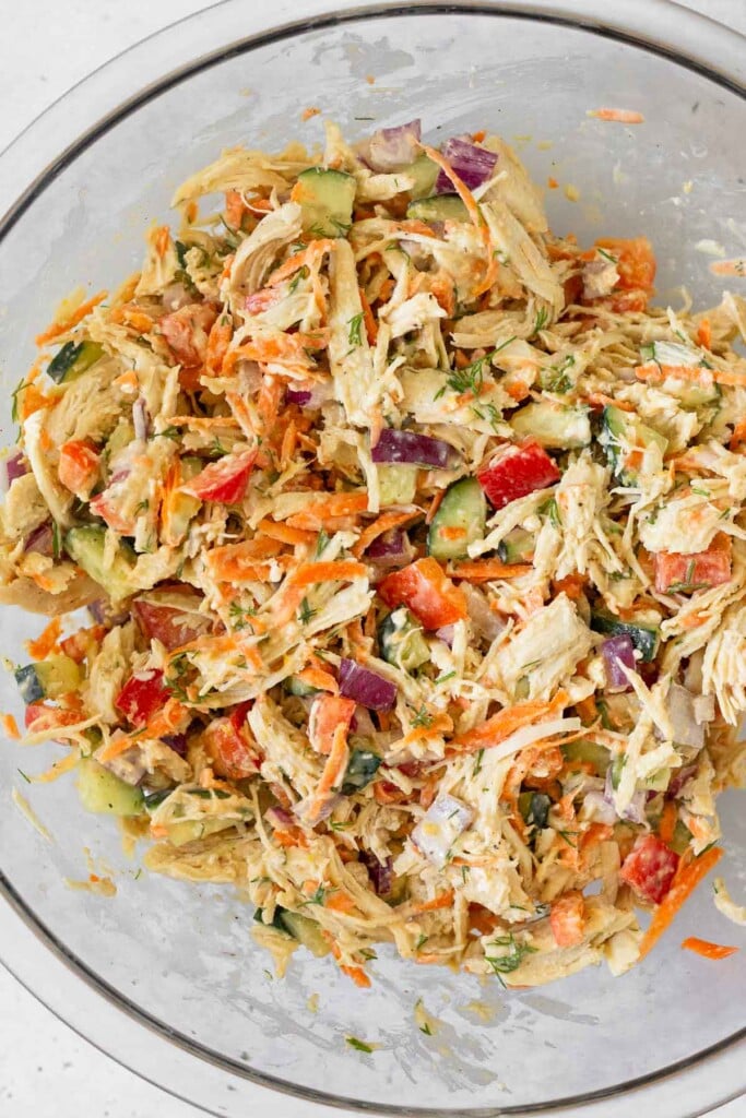 A bowl of shredded chicken mixed with bell peppers, carrots, cucumber, red onion, and dill.