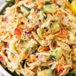 Hummus chicken salad overtop greens in a white bowl.