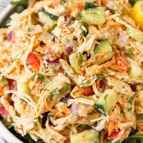 Hummus chicken salad overtop greens in a white bowl.