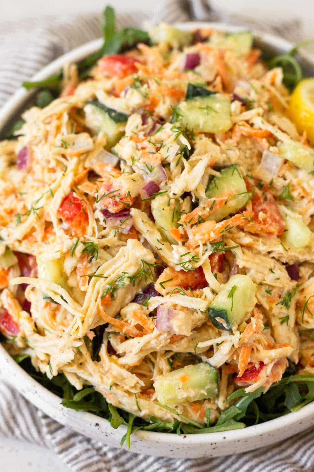 Hummus chicken salad overtop greens in a white bowl.