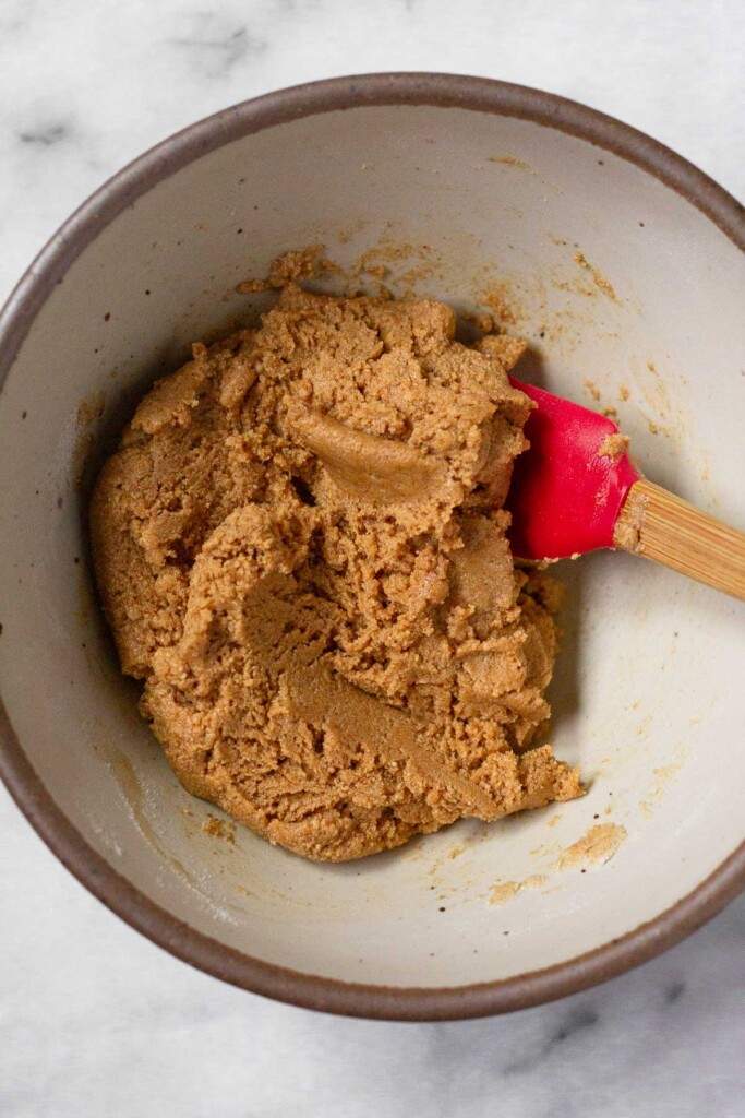 Peanut butter dough in a white bowl with a red spatula in it.