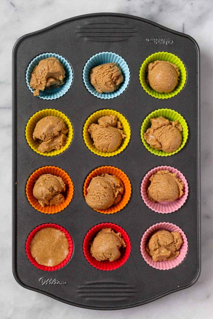 Mini muffin tin with colorful mini silicone liners in it with each one being filled a dough.