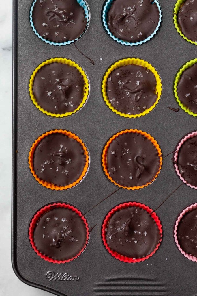 Mini peanut butter cups in silicone liners in baking dish. They are sprinkled with sea salt.