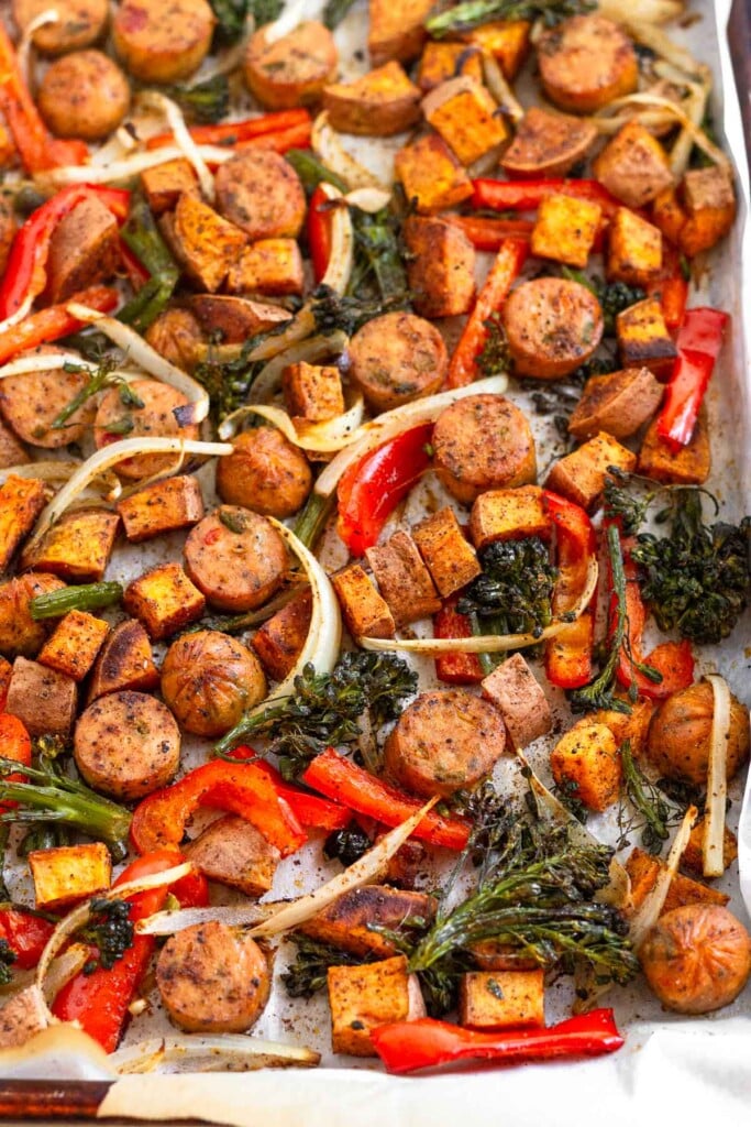 Sheet pan filled with roasted sliced chicken sausages, roasted sweet potatoes, roasted sliced peppers, roasted sliced onions, and roasted broccoli.