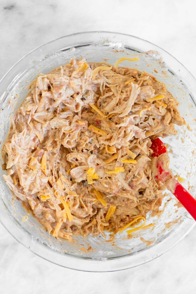 Bowl with a mixture of chicken, yogurt, seasonings, and shredded cheese.