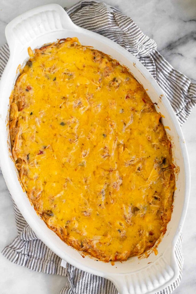 Chicken cheese dip in a white baking dish on a striped kitchen towel.