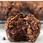 Chocolate oatmeal muffin with a bite taken out of it with some mini chocolate chips around it. Behind it is a rack of more muffins.