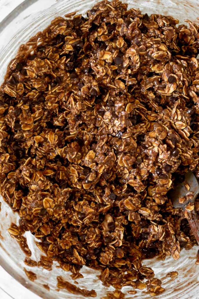 Glass bowl with a chocolate batter with rolled oats and chocolate chips in it. A fork is in the bowl.
