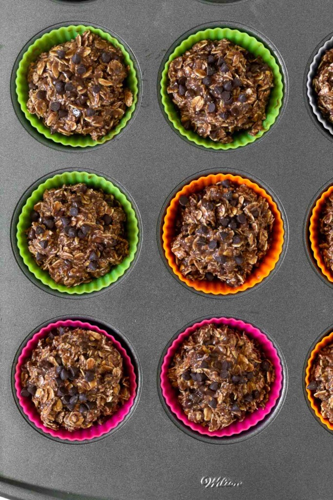 Muffin tin filled with colorful silicon liners with chocolate oatmeal banana muffins muffins in them before they are baked.