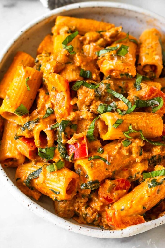 Close up of cottage cheese pasta topped with fresh basil and grated parmesan and in white bowl.