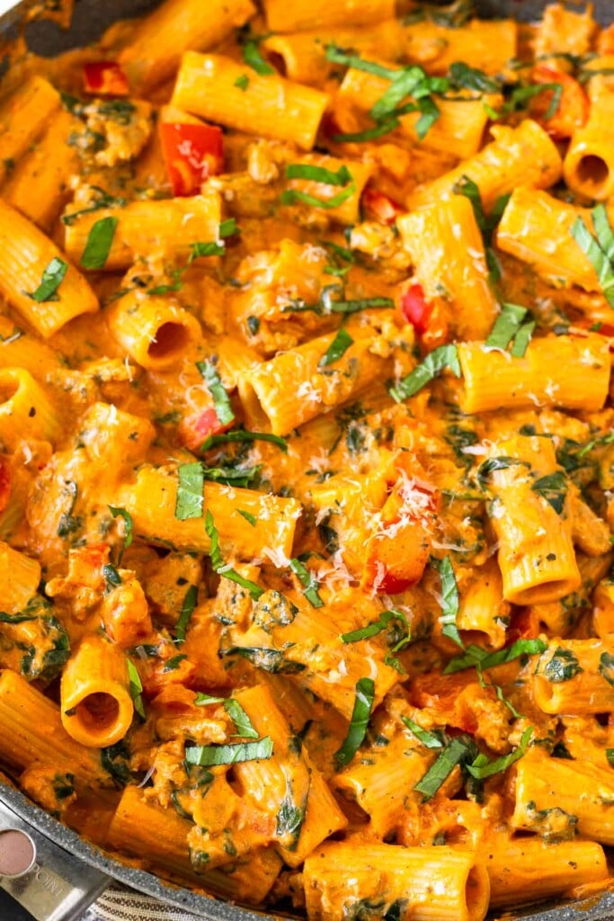 Pasta with ground turkey and veggies mixed with a creamy cottage cheese pasta sauce in a large skillet. It is garnished with fresh basil and grated parmesan cheese.