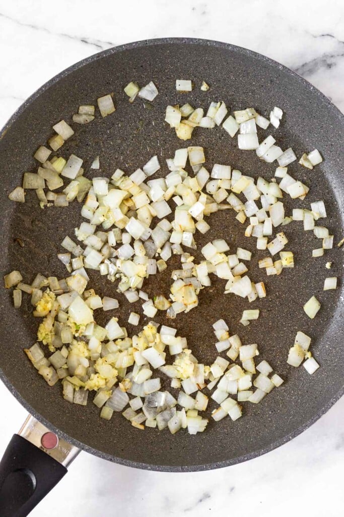 Large skillet filled with sautéed onion and garlic.
