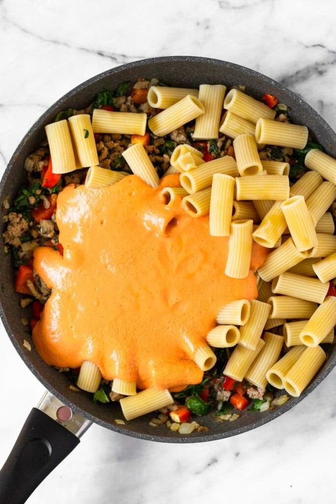 Large skillet filled with a sautéed veggies and ground turkey, cooked pasta, and pasta sauce.
