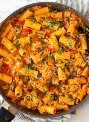Cottage cheese pasta with ground turkey and veggies in a large skillet garnished with basil and parmesan cheese. The skillet is on top of a striped towel.