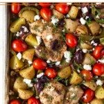 Greek sheet pan chicken with roasted potatoes, peppers, and onions, cherry tomatoes, Kalamata olives, and feta. It is garnished with fresh dill.