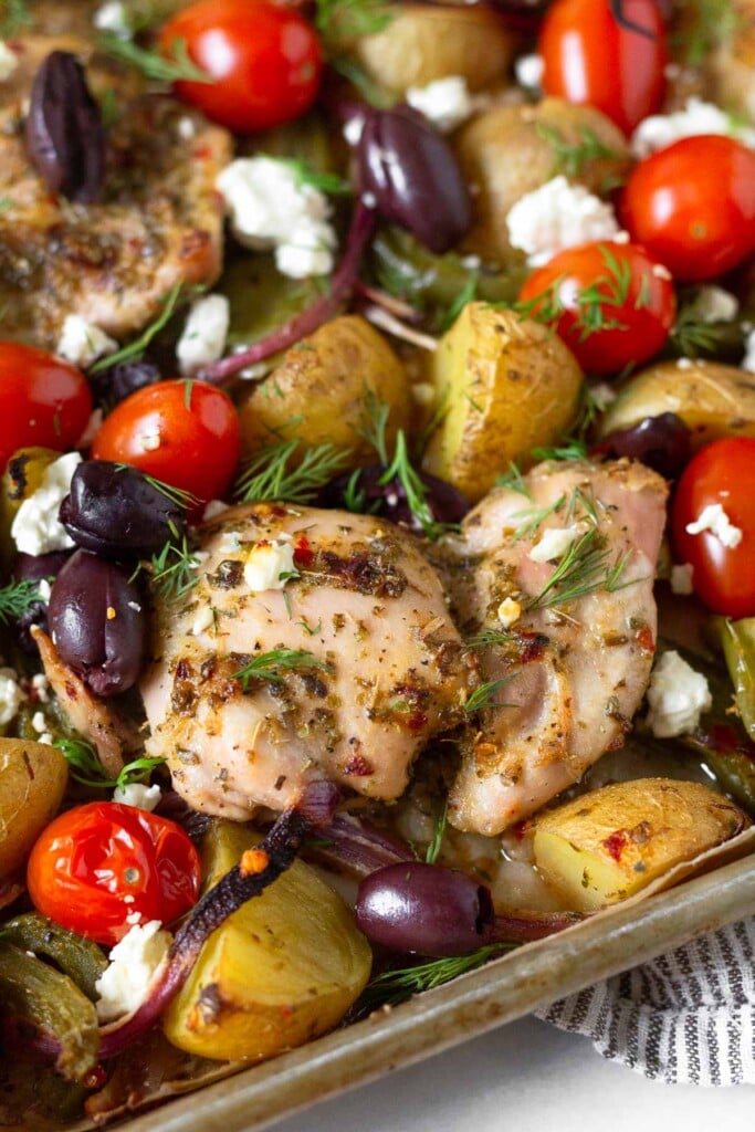 Sheet pan greek chicken with potatoes, peppers, onions, tomatoes, olives, and feta cheese garnished with fresh dill.