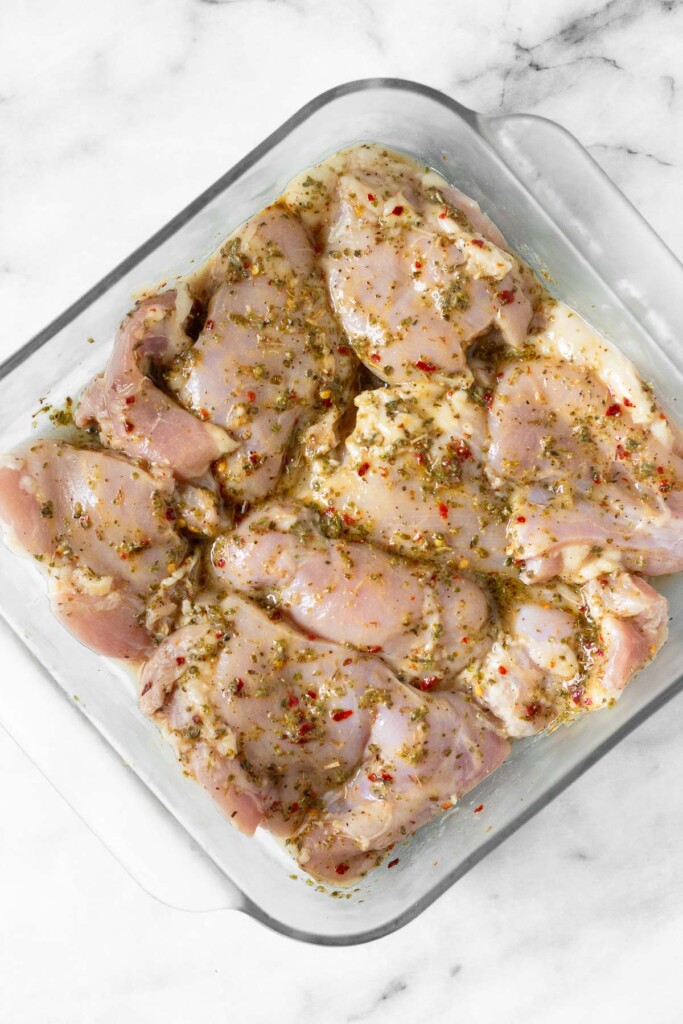 Raw chicken thighs in a baking dish covered with marinade.