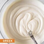 Greek yogurt frosting in a glass bowl with a small metal whisk in it.