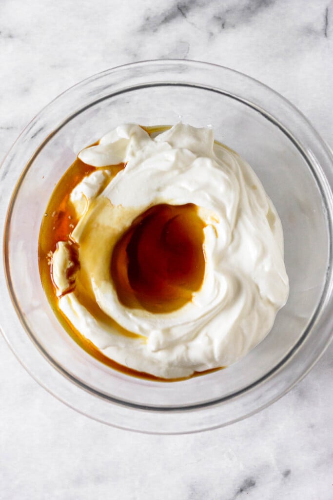 Glass bowl with greek yogurt with a pool of maple syrup on top.