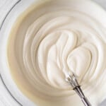 Greek yogurt frosting in a glass bowl with a small metal whisk in it.