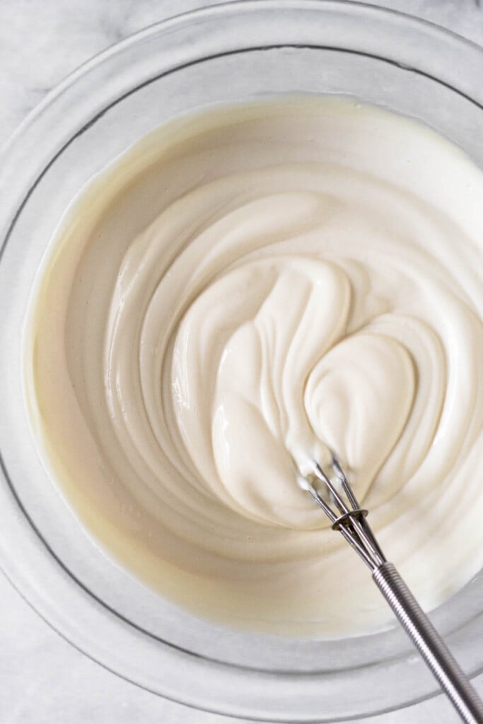 Greek yogurt frosting in a glass bowl with a small metal whisk in it.