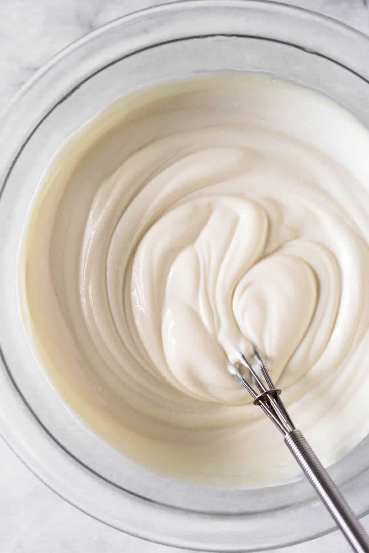Greek yogurt frosting in a glass bowl with a small metal whisk in it.