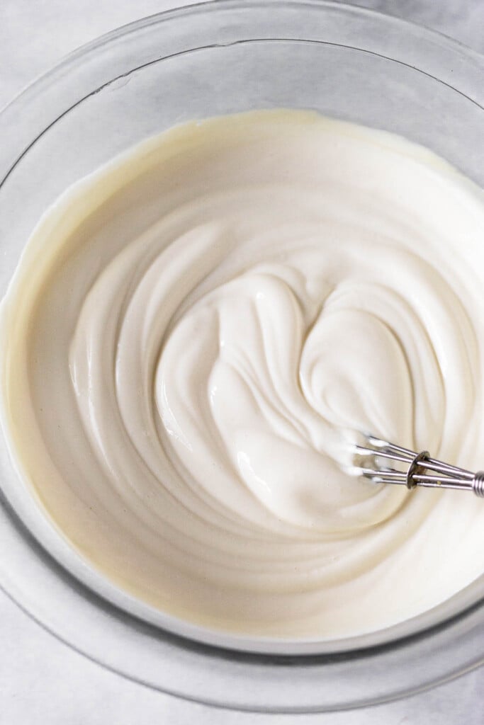 Greek yogurt icing in a glass bowl with a small metal whisk in it.