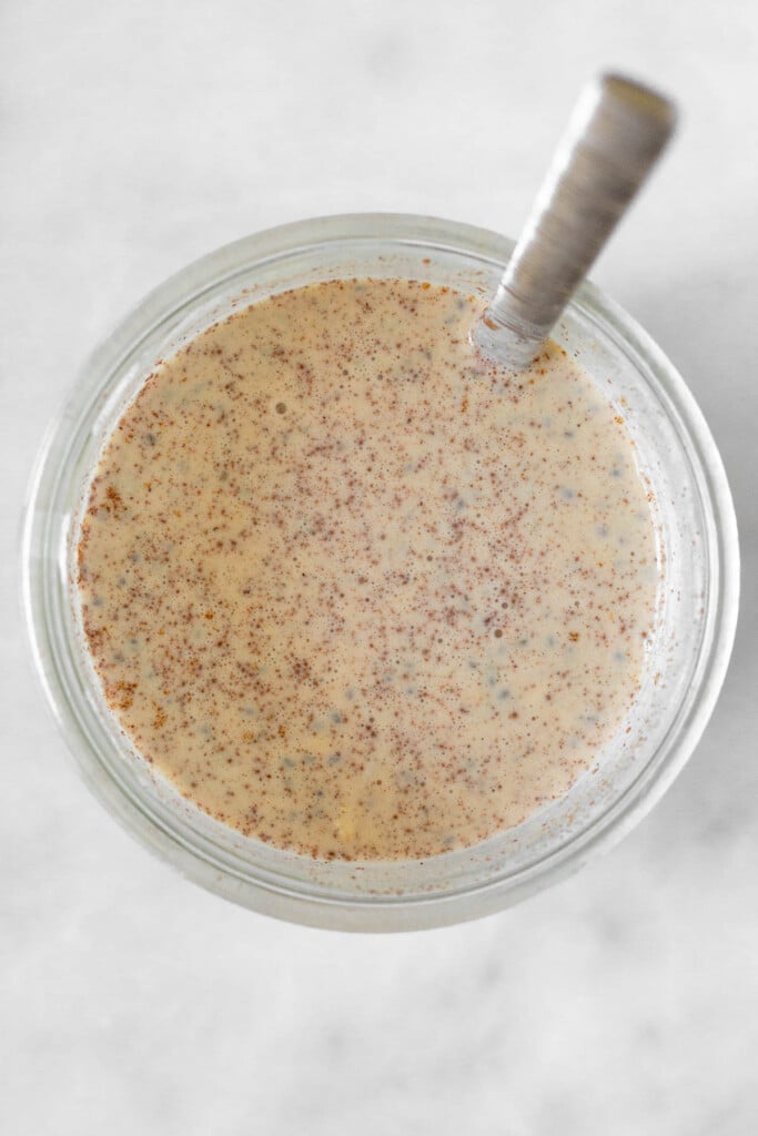 Overhead shot of a jar filled with a liquid mixture of milk, cinnamon, rolled oats, and chia seeds.