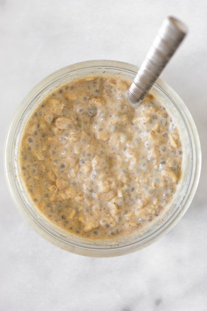 Overhead shot of a jar filled with a creamy mixture of rolled oats, chia seeds, and cinnamon with a spoon in it.