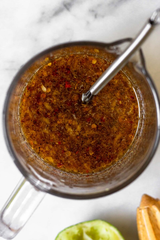 Measuring cup filled with stir fry sauce with a small whisk in it. Next to it is half a lime and a citrus reamer.