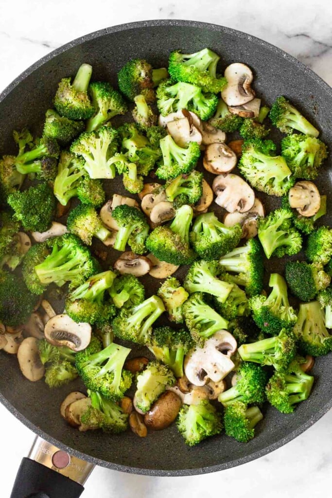 Large skillet filled with sautéed broccoli florets and sliced mushrooms.