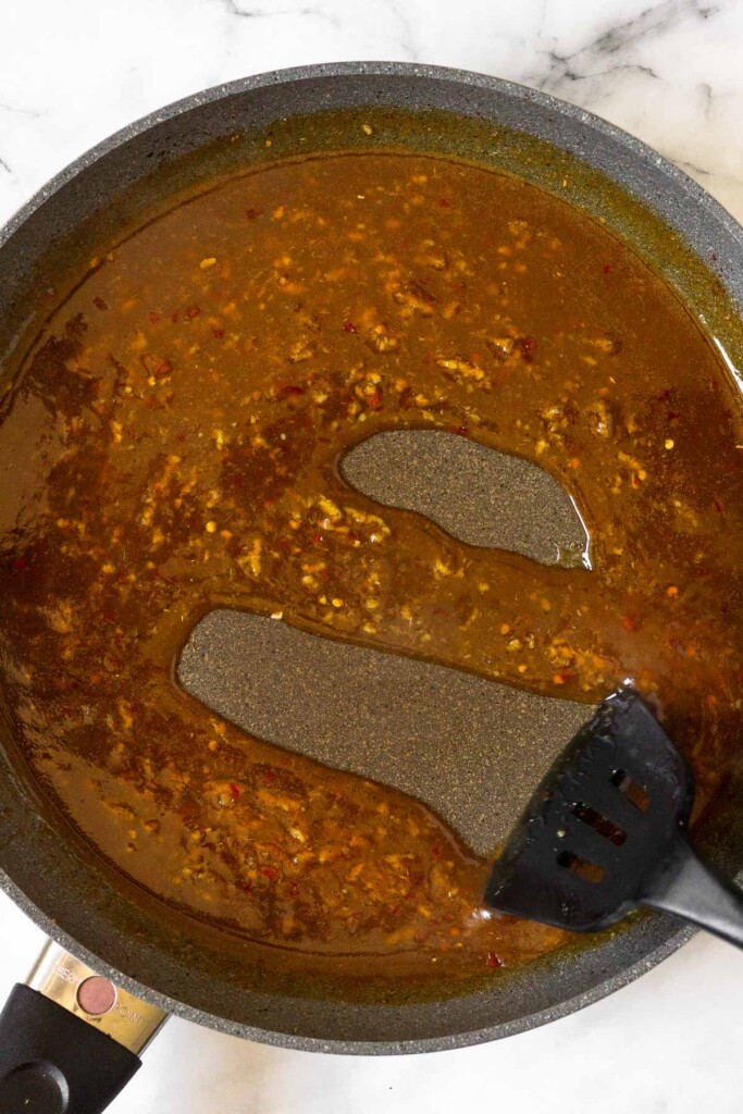 Large skillet filled with a thick stir fry sauce with a spatula running through it through it and leaving a clean line behind it.