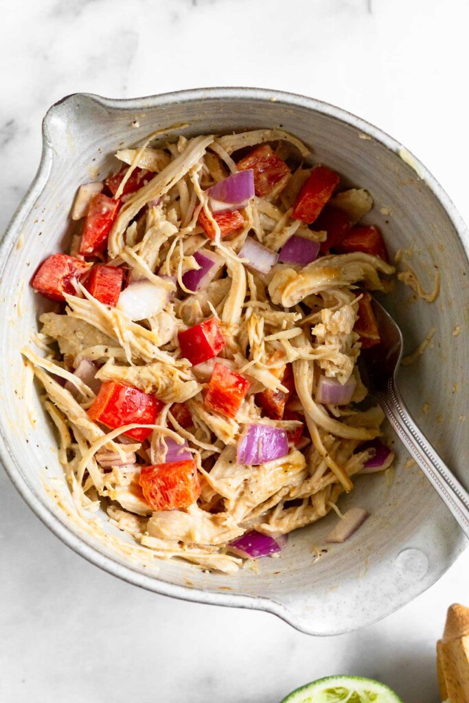 Chipotle chicken salad with peppers and onions in a bowl with a fork in it. Next to the bowl is half a juiced lime and a wooden reamer.